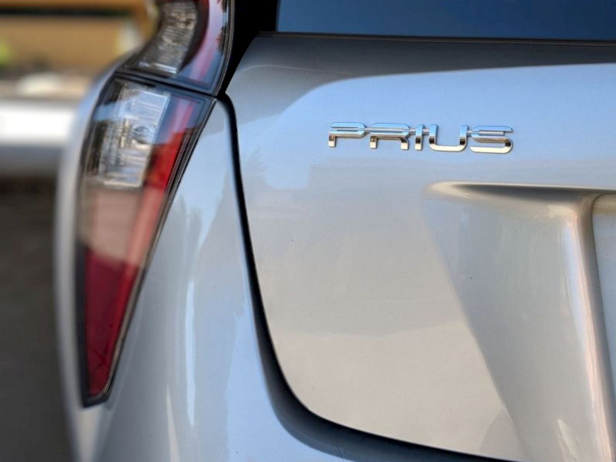 The image shows the rear end of a silver Toyota Prius, featuring the tail light and the Prius emblem on the trunk.