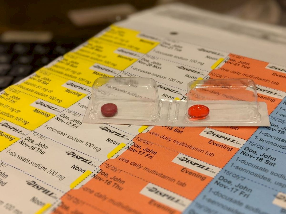 The image shows a medication schedule chart with various colored sections and two blister packs containing pills placed on the chart.