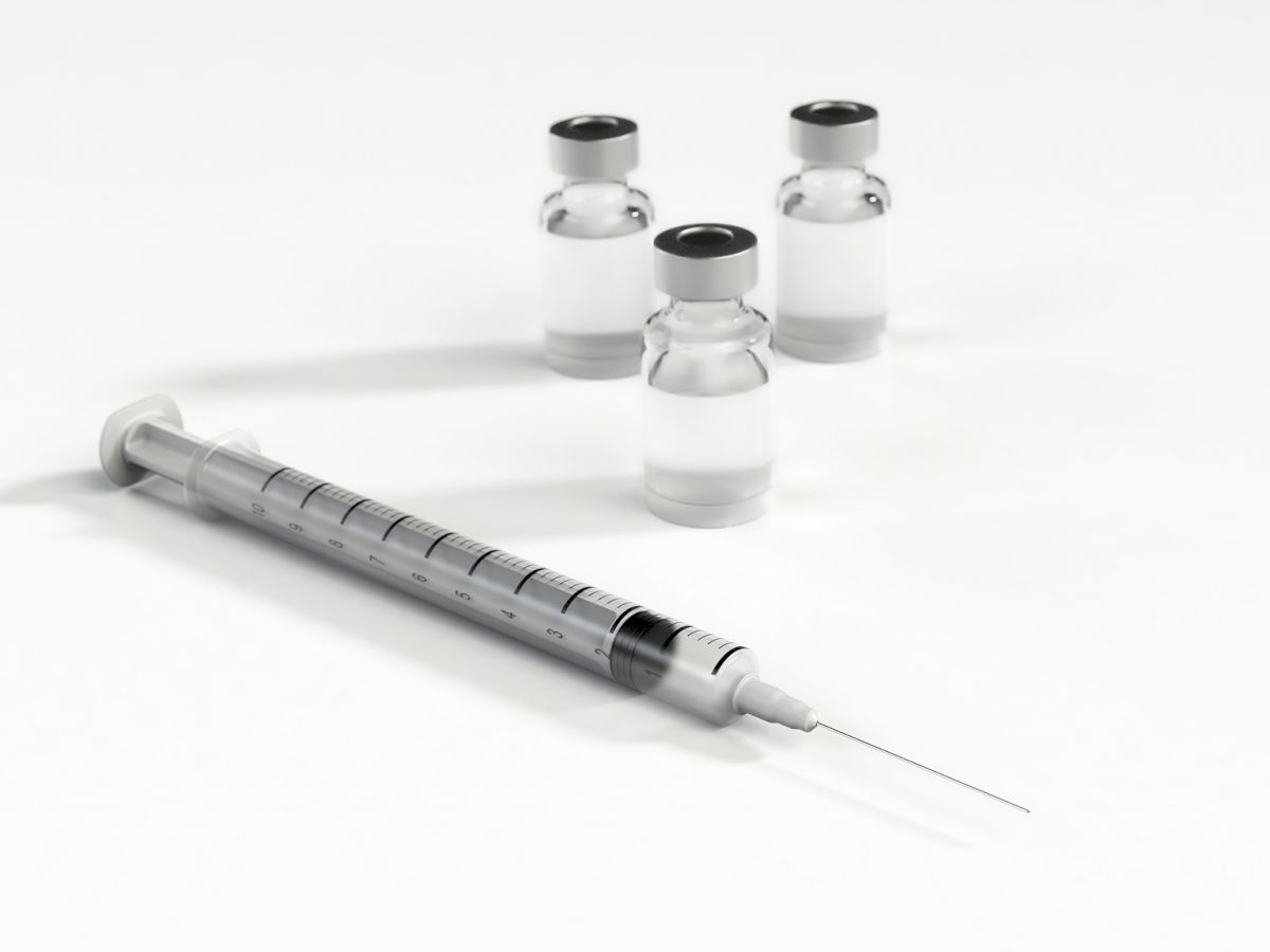 The image shows a syringe lying on a surface next to three small, clear vials containing a liquid.