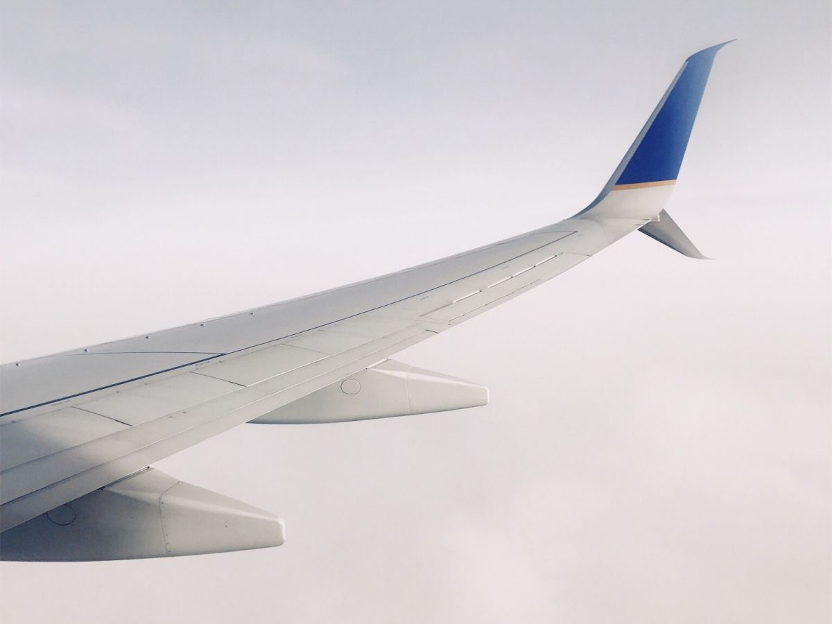 An airplane wing with a blue tip is seen against a backdrop of a cloudy, overcast sky.