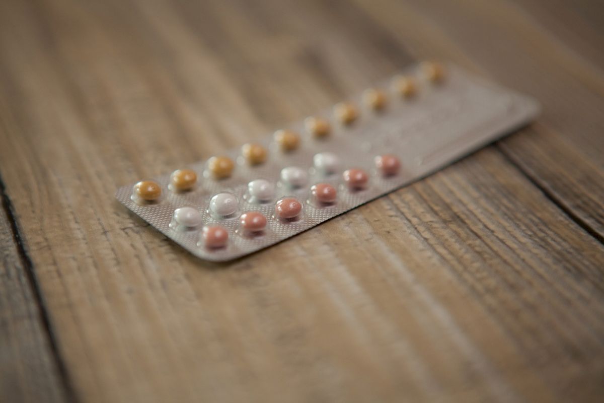 The image shows a blister pack of birth control pills lying on a wooden surface. The pack contains pills of different colors.