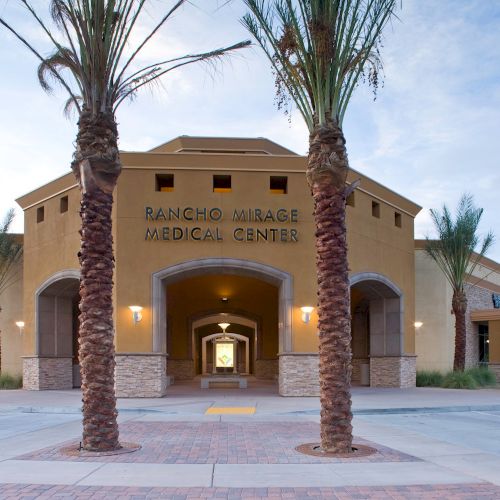 The image shows the entrance of Rancho Mirage Medical Center, surrounded by palm trees and featuring an archway.