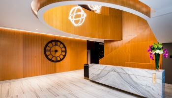 A modern, stylish reception area with a spiral design, large wall clock, marble desk, and decorative flowers under artistic lighting fixtures.