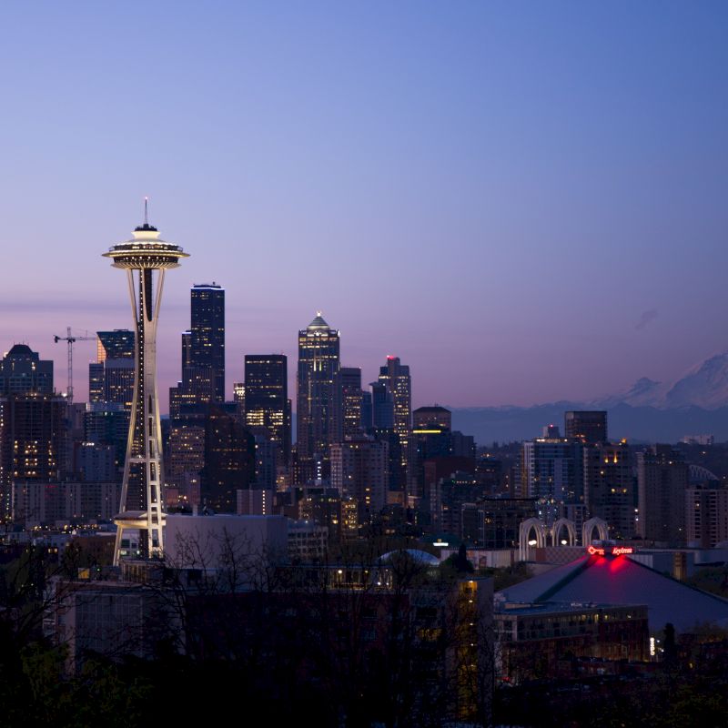 The image features the Seattle skyline at dusk, including the Space Needle, with Mount Rainier visible in the background.