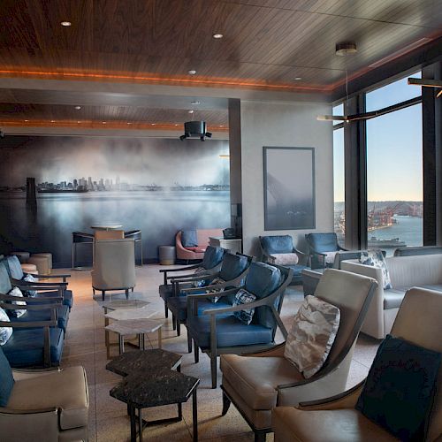 A modern, comfortable lounge area with many seats, large windows offering a scenic view, and soft lighting illuminating the room.