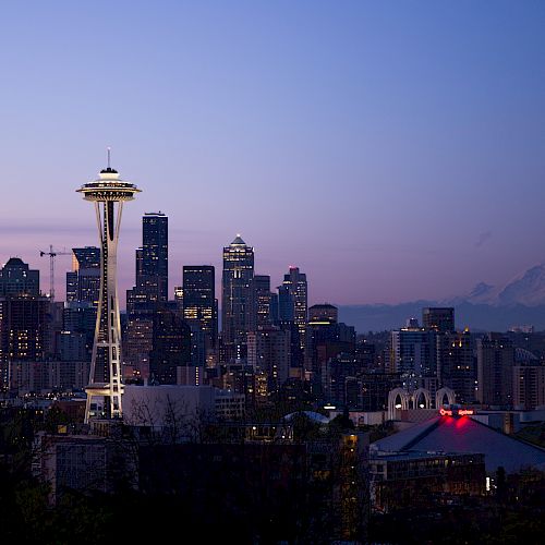 A cityscape of Seattle at dusk featuring the Space Needle, downtown skyscrapers, and Mt. Rainier in the background with a clear sky.