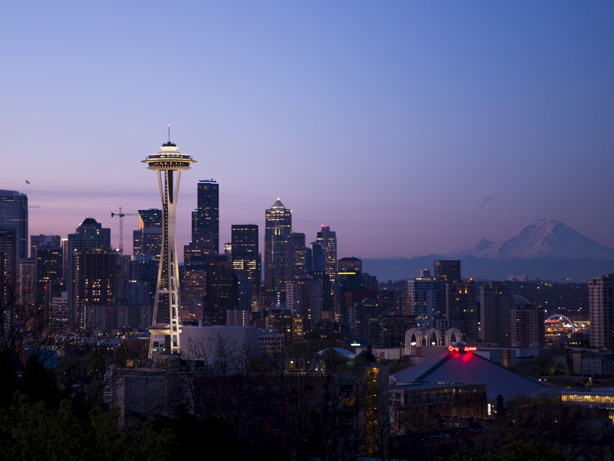 This image shows the Seattle skyline at dusk, featuring the Space Needle and surrounding high-rise buildings, with Mount Rainier visible in the background.