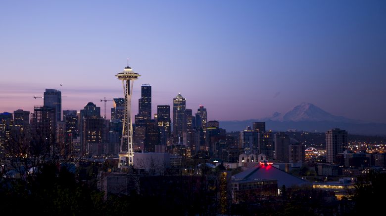 This image shows the Seattle skyline at dusk, featuring the Space Needle and surrounding high-rise buildings, with Mount Rainier visible in the background.