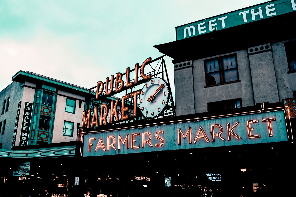 This image shows the iconic Public Market Center entrance sign at Pike Place Market in Seattle, with "Farmers Market" and "Meet the Producer" signage visible.