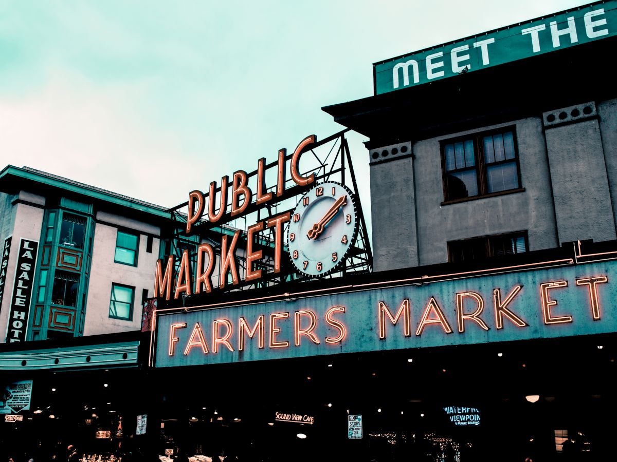 This image shows the iconic Public Market Center entrance sign at Pike Place Market in Seattle, with "Farmers Market" and "Meet the Producer" signage visible.