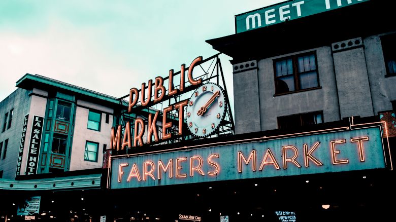 This image shows the iconic Public Market Center entrance sign at Pike Place Market in Seattle, with "Farmers Market" and "Meet the Producer" signage visible.