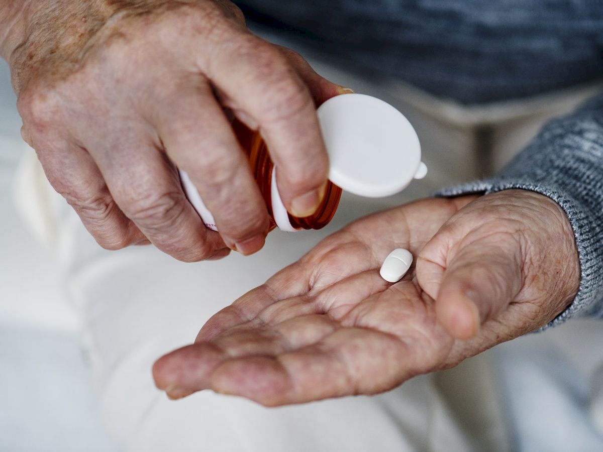 An elderly person is holding a pill bottle and dispensing a white pill into their hand.